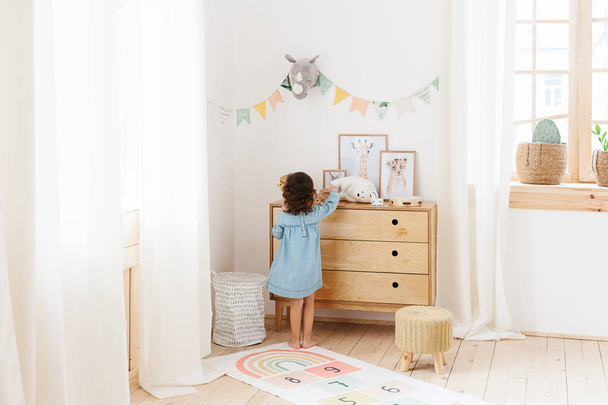 Little girl wearing light blue dress playing in children room scandinavian style. - Foto, Imagen