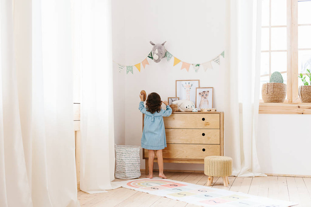 Little girl wearing light blue dress playing in children room scandinavian style. - Фото, изображение