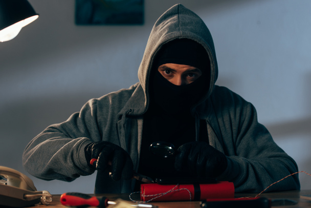 Террорист в маске и перчатках делает бомбу и смотрит в камеру
 - Фото, изображение