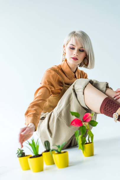 selective focus of beautiful stylish girl sitting with flower transplants on white - Foto, immagini