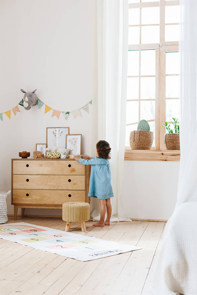 Niña con vestido azul claro jugando en la habitación de los niños de estilo escandinavo
. - Foto, Imagen