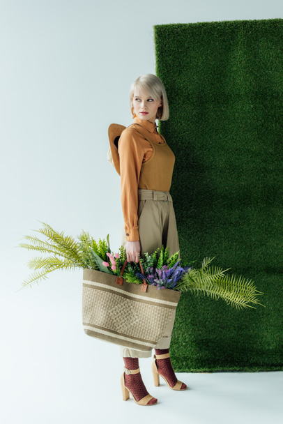 beautiful stylish girl holding bag with fern and flowers on white with green grass  - Foto, Bild