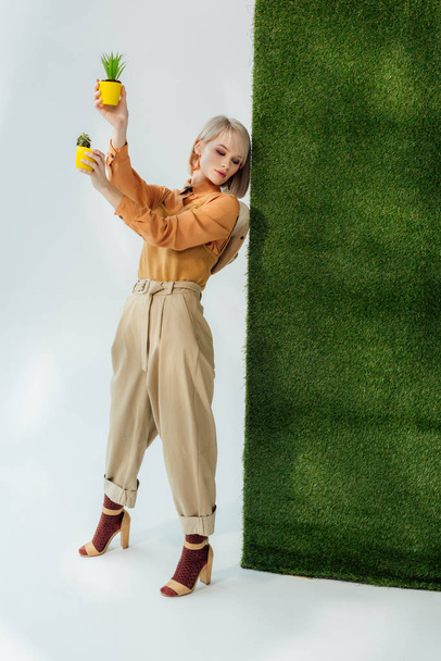 beautiful stylish blonde girl holding flower pots on grey with green grass  - Valokuva, kuva
