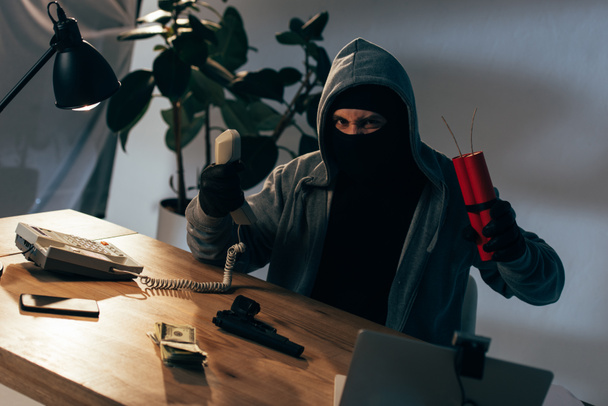 Terrorista enojado con máscara y guantes sosteniendo el auricular y la dinamita
 - Foto, Imagen