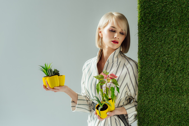 schöne stylische junge Frau mit Blumentöpfen auf grau mit grünem Gras  - Foto, Bild