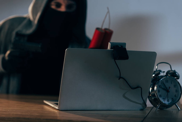 Terrorist in mask holding dynamite while using laptop in dark room - Photo, Image