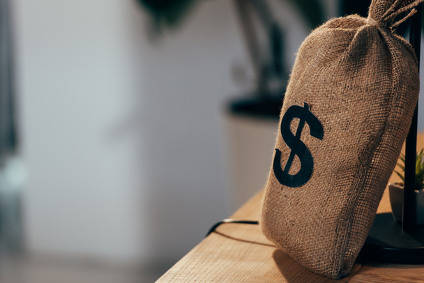 Грошова сумка зі знаком долара, що стоїть на дерев'яному столі
 - Фото, зображення