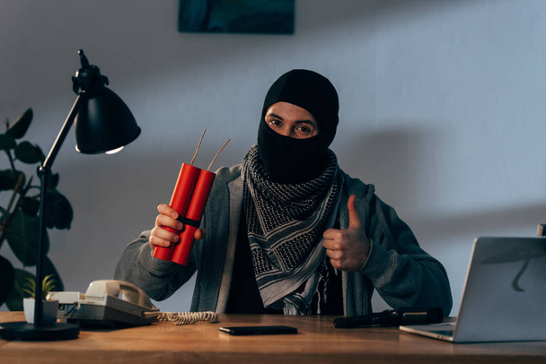 Terrorist mit Maske hält Dynamit in der Hand und zeigt Daumen nach oben - Foto, Bild
