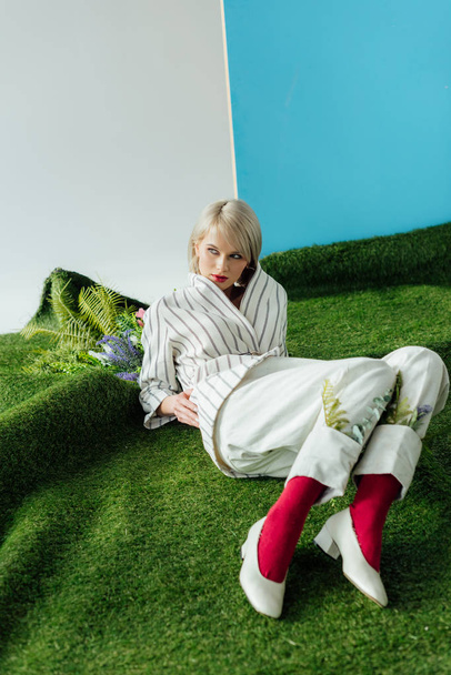 piękna stylowa dziewczyna Blondynka pozowanie na sztucznej murawie z paproci i kwiaty - Zdjęcie, obraz