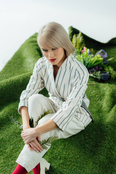 krásná stylová blond dívka pózuje na umělé trávě s kapradí listy - Fotografie, Obrázek