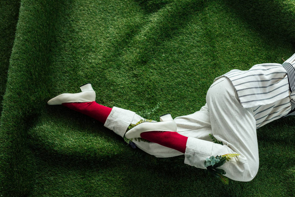 cropped view of woman in white pants with green leaves and stylish shoes lying on artificial grass - Фото, зображення