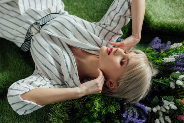 beautiful stylish girl with eyes closed posing on artificial grass with fern and flowers - Foto, Imagen