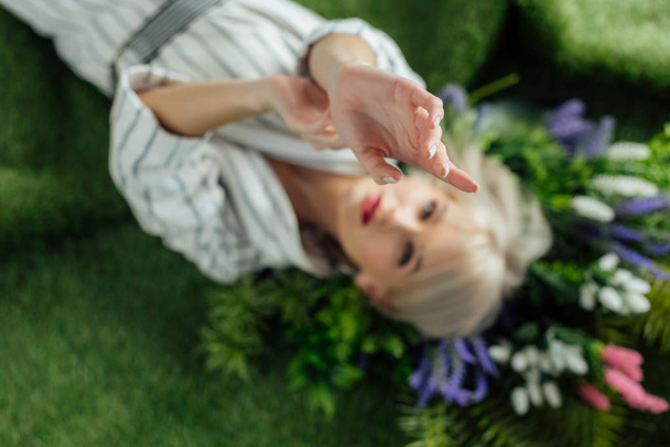 chica con estilo con las manos extendidas acostado en césped artificial con plantas
 - Foto, Imagen