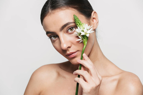 Healthy attractive brunette woman standing isolated holding flower plant near her face - Фото, зображення