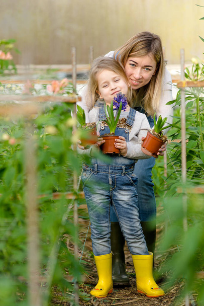 Una donna con una piccola figlia tiene fiori in vaso in una serra
. - Foto, immagini