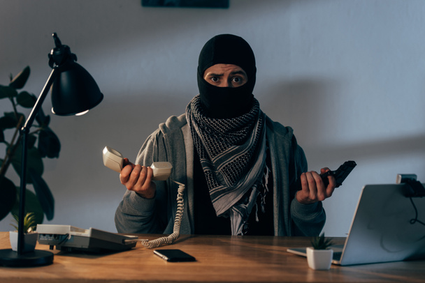 Разочарованный террорист в маске с пистолетом и телефоном
 - Фото, изображение
