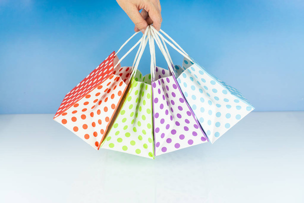 Woman holds four colorful dotted paper bags in her hand, blue background and copy space - Foto, immagini