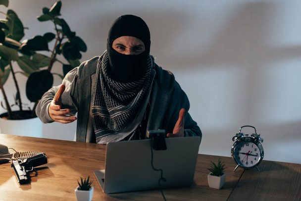 Злий терорист в чорній масці жестикулює на веб-камеру в кімнаті
 - Фото, зображення