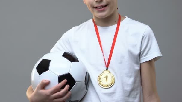 Boy with soccer ball and first place medal standing against grey background - Кадры, видео