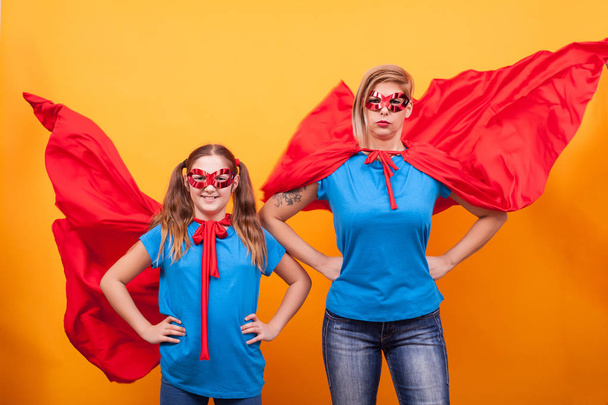 Mutter und Tochter kleiden sich wie Superhelden mit ihren roten Umhängen in der Luft über gelbem Backgtound - Foto, Bild