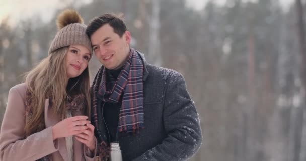 Casal feliz segurando xícaras de chá quente durante a paisagem de inverno. Jovem casal apaixonado em umas férias de inverno, de pé ao lado de uma árvore e beber uma xícara de chá quente
 - Filmagem, Vídeo