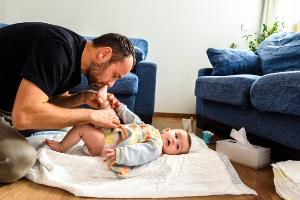Padre cambiando el pañal de su bebé mientras lo acaricia affectiona
 - Foto, Imagen