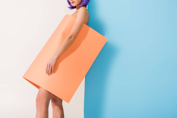 cropped view of girl covered in coral paper sheet posing on blue and white with copy space - Foto, Imagen