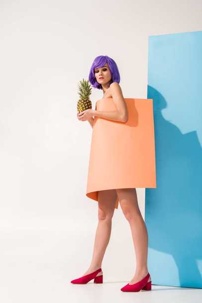 beautiful young woman with purple hair covered in coral paper sheet holding pineapple on blue and white - Photo, Image