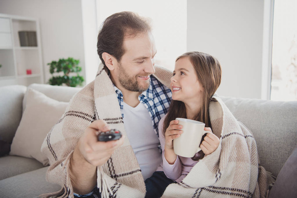 Portrait of his he her she nice cute lovely attractive cheerful lovable pre-teen girl handsome bearded dad daddy sitting on divan watching cartoon drinking cacao in modern light white interior room - Foto, Imagen