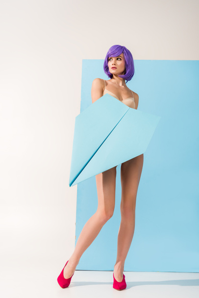 beautiful young woman with purple hair posing with paper plane on blue and white - Foto, imagen