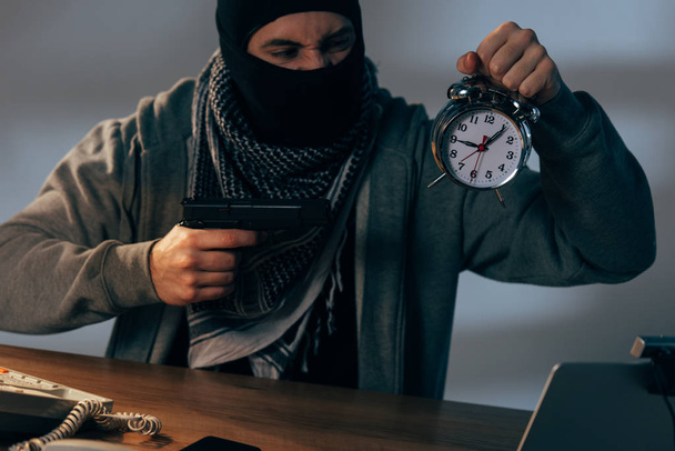 Агресивний терорист тримає пістолет і будильник за столом
 - Фото, зображення
