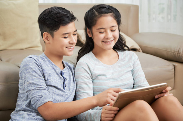 Sonriendo hermano y hermana de raza mixta leyendo algo en la tableta
 - Foto, imagen