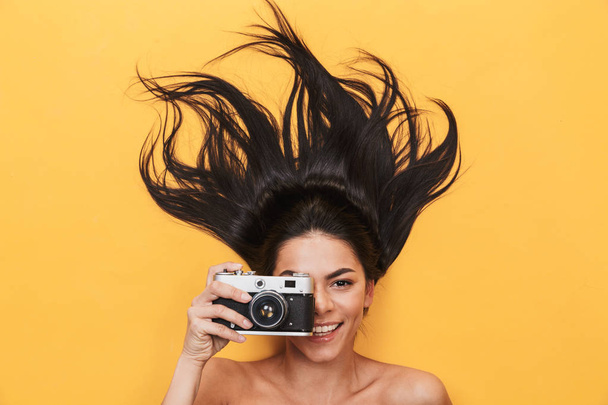 Happy young woman lies isolated on yellow background holding camera photographing. - Fotografie, Obrázek