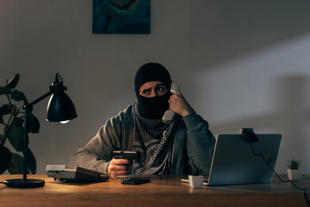 Terrorista preocupado con máscara hablando por teléfono y portando armas
 - Foto, Imagen