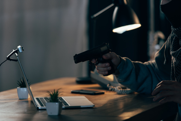 Обрезанный вид преступника в маске, нацеленный пистолет на экран ноутбука
 - Фото, изображение