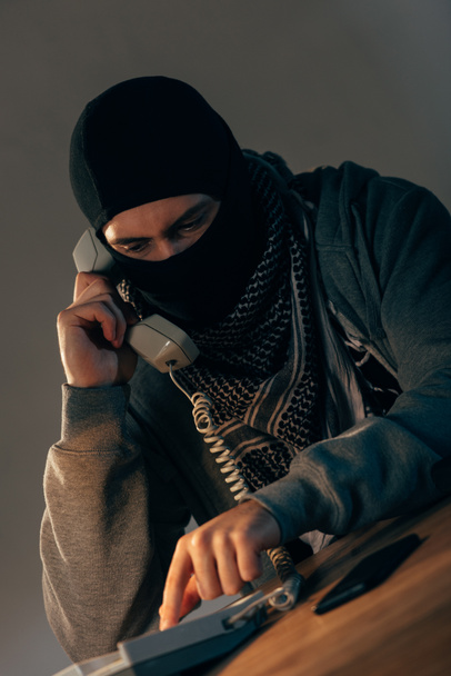 Террорист в черной маске разговаривает по телефону в номере
 - Фото, изображение
