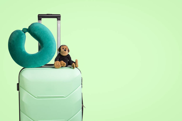 Plastic suitcase with wheels, soft toy, travel pillow, green background. Travel concept for children, visit to relatives, trip to camp - Photo, Image