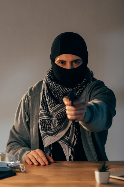 Schwerverbrecher mit schwarzer Maske zielt mit Waffe auf Kamera - Foto, Bild