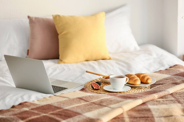 Wicker mat with delicious breakfast and laptop on bed - Foto, imagen