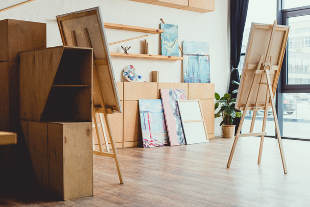 spacious light painting studio with wooden floor, cabinets, shelves, easels and paintings - 写真・画像