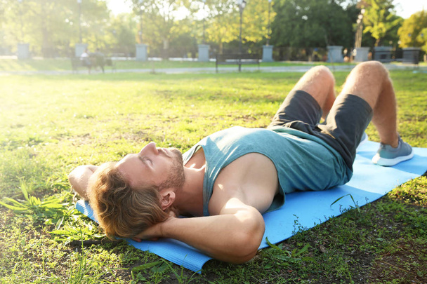 Beau jeune homme allongé sur un tapis de yoga dans le parc
 - Photo, image