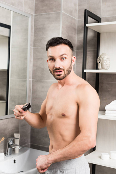 surprised shirtless man holding trimmer while standing in bathroom  - Photo, Image