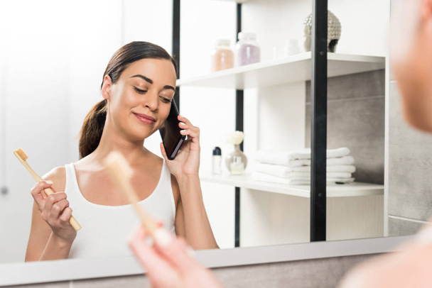 selective focus of happy brunette woman holding toothbrush while talking on smartphone in bathroom  - Photo, image