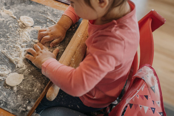 toddler girl rolls dough for pirogi with her grandmother in the  kitchen by the home - Φωτογραφία, εικόνα