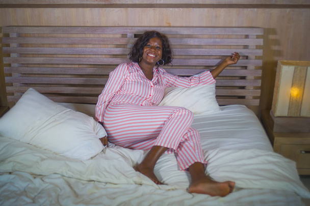young happy and beautiful black African American woman in pajamas lying relaxed and playful on bed smiling cheerful and positive waking up in the morning optimistic and fresh - Foto, Imagen