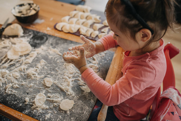 toddler girl rolls dough for pirogi with her grandmother in the kitchen by the home - 写真・画像