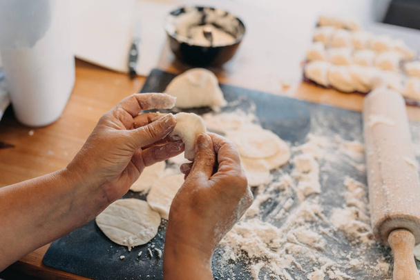 closeup hands of grandmother preparing dough and making pirogi in the kitchen by the home - Valokuva, kuva