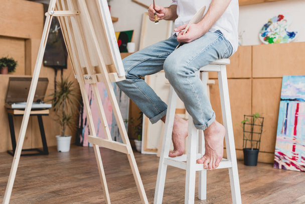 vista parcial del artista descalzo sentado en la silla alta en el estudio de pintura
 - Foto, Imagen