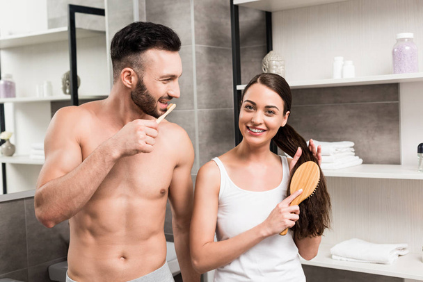 陽気な男の浴室で髪をブラッシングの魅力的なガール フレンドを見て  - 写真・画像
