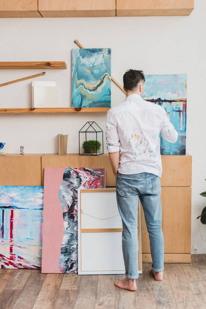 back view pf barefoot artist in white shirt and blue jeans standing in painting studio - Foto, imagen